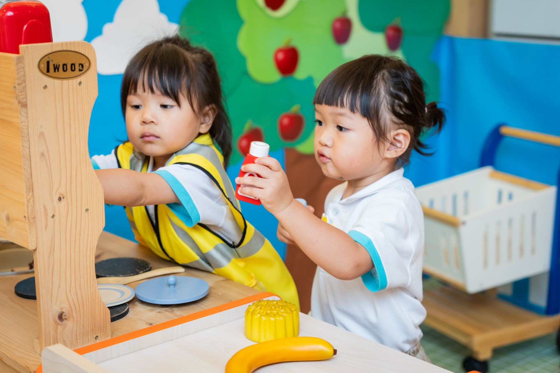  Two girls playing in the indoor playground role-play area, dressed as shopkeepers